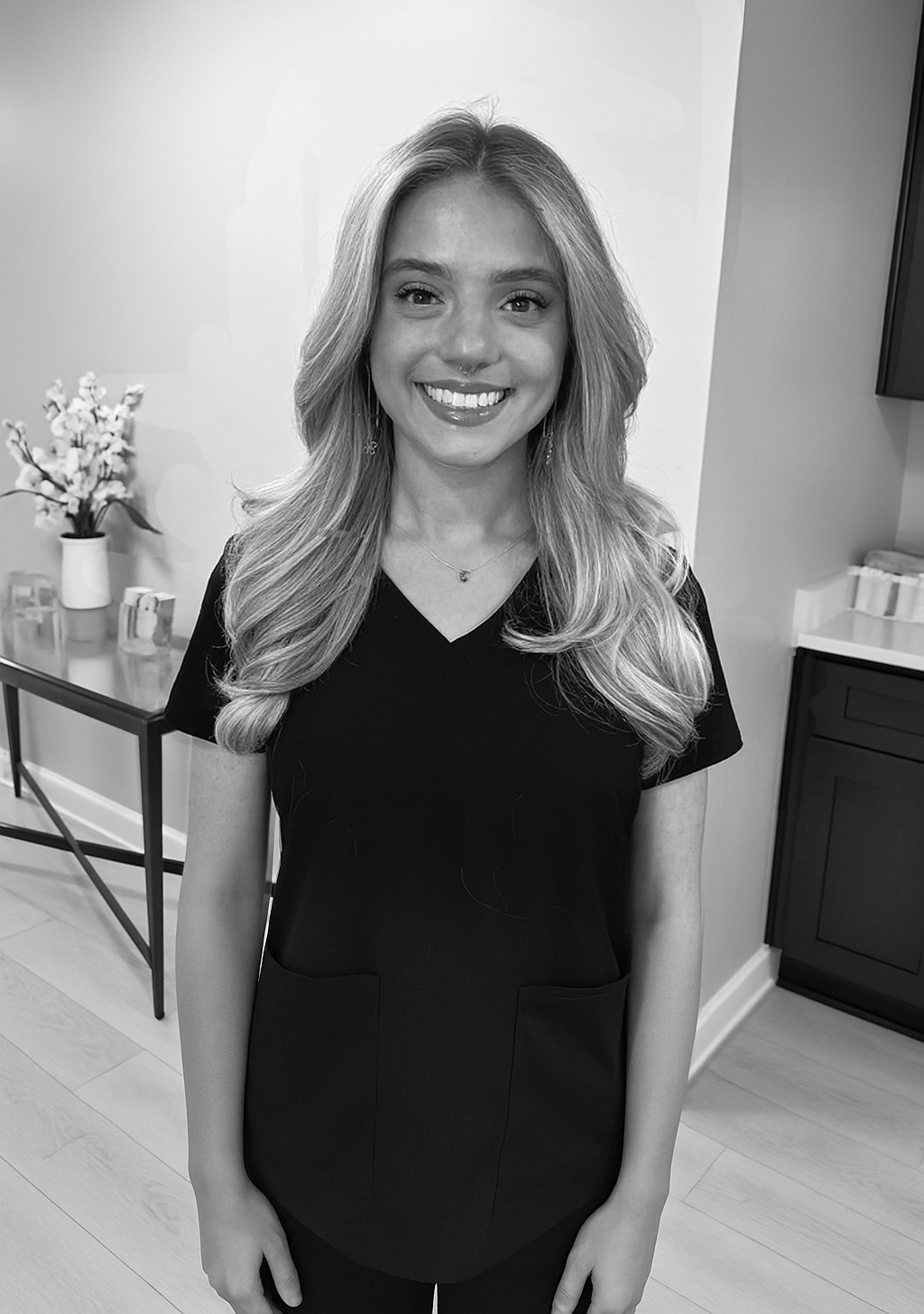 A black and white portrait of a smiling woman leaning against a railing with foliage.